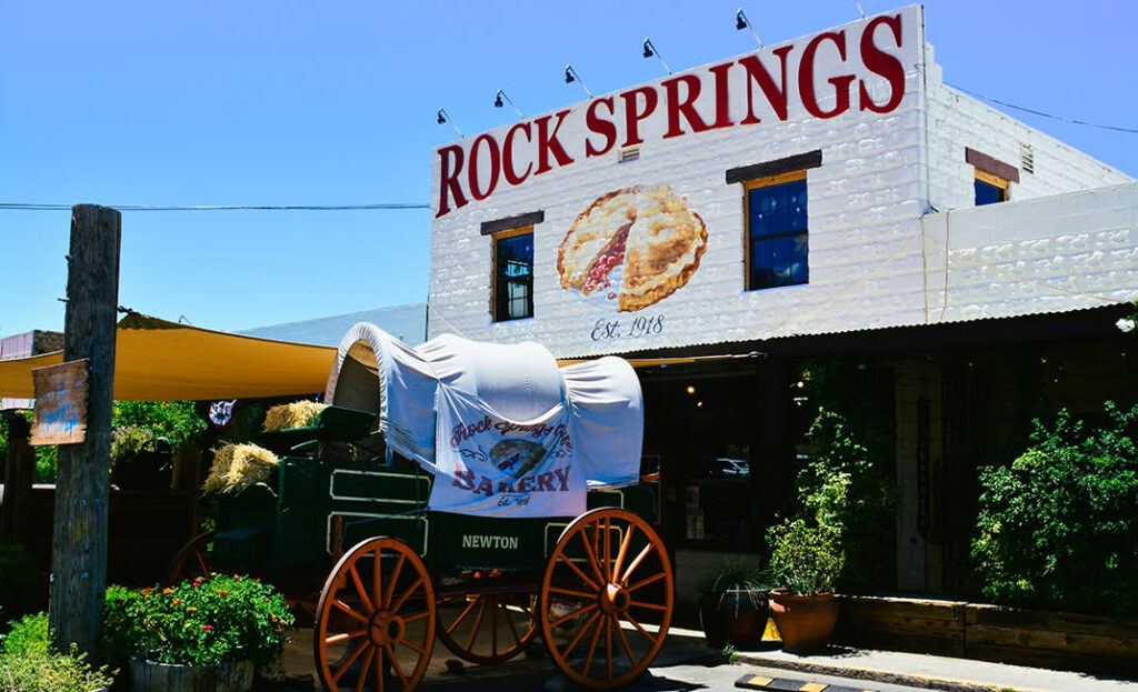 A covered wagon is parked in front of the Rock Springs Café, which has a large sign and a pie illustration on its facade.