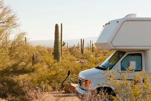 A white RV is parked in a desert landscape with cacti and sparse vegetation under a clear sky.